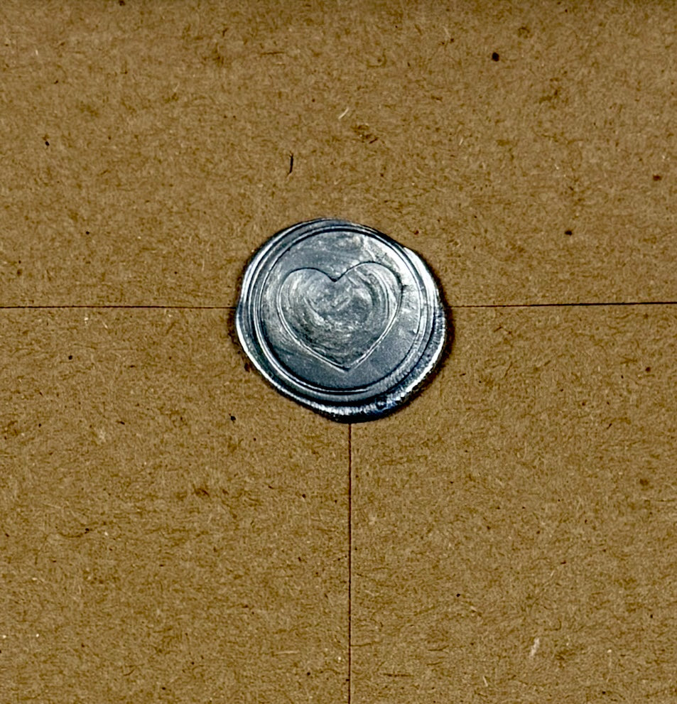 Metallic wax seal with heart design stamp on a brown envelope